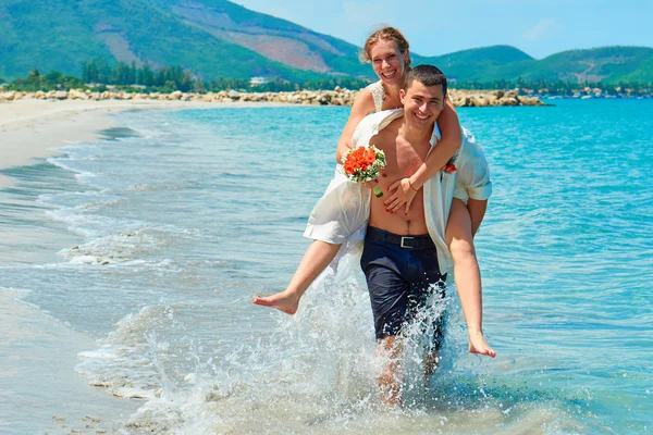 Glückliche Braut und Bräutigam laufen an einem wunderschönen tropischen Strand — Stockfoto