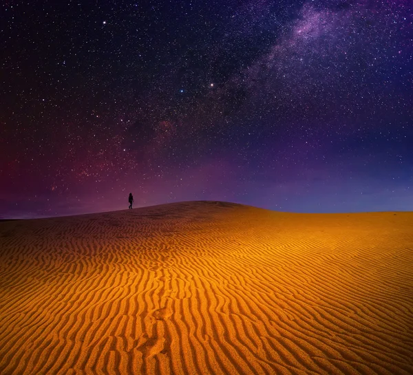 Um mochileiro está andando entre dunas de areia sob o céu estrelado — Fotografia de Stock