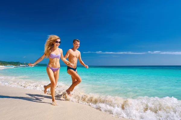 Feliz pareja corriendo a través de olas en vacaciones en la playa — Foto de Stock