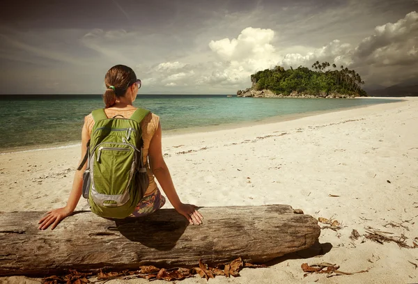 Junge Frau mit Rucksack entspannt sich an der Küste und blickt auf eine Insel — Stockfoto