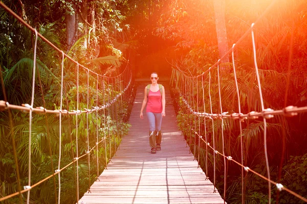 Happy woman hiker crossing suspension bridge in sunlight. — Stock Photo, Image
