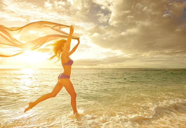Glückliche unbeschwerte Frau, die im Sonnenuntergang am Strand läuft. — Stockfoto