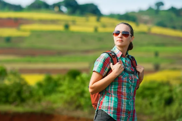 Jovem mulher mochileiro caminha no fundo de campos coloridos — Fotografia de Stock