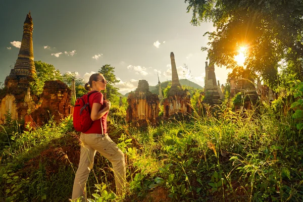 Female traveler with backpack walking and looks at sunset among — Stock Photo, Image