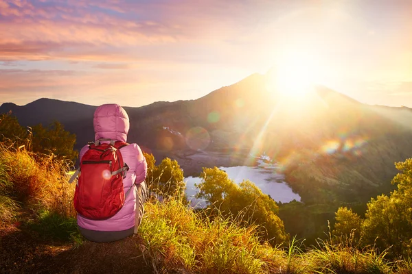 Kvinna med backpacker njuter sunrise utsikten på höga berg. — Stockfoto