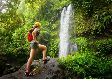 young woman backpacker looking at the waterfall in jungles. clipart