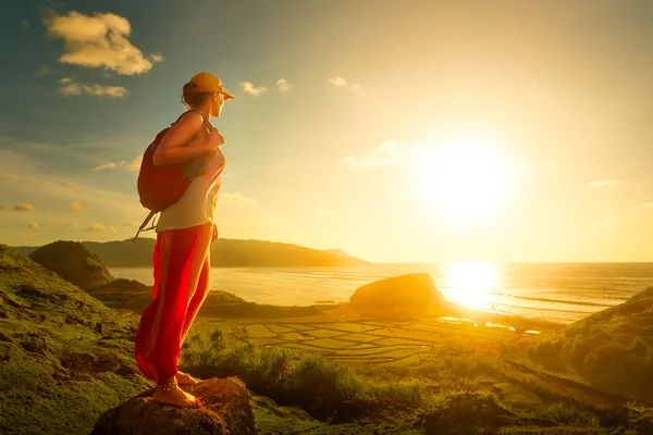 Πεζοπόρος γυναίκα στέκεται στην κορυφή της και να απολαύσετε το ηλιοβασίλεμα πάνω από τη θάλασσα. — Φωτογραφία Αρχείου
