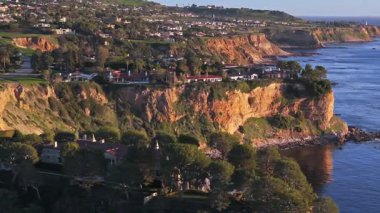 Güneş batarken Palos Verdes kıyı şeridinin nefes kesen hava yörüngesi görüntüsü okyanusun üzerindeki engebeli kayalıkları ve evleri aydınlatan Palos Verdes Evleri, Kaliforniya