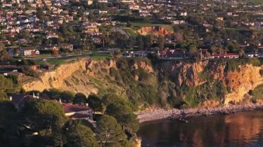 Güneş batarken Palos Verdes kıyı şeridinin nefes kesen hava yörüngesi görüntüsü okyanusun üzerindeki engebeli kayalıkları ve evleri aydınlatan Palos Verdes Evleri, Kaliforniya