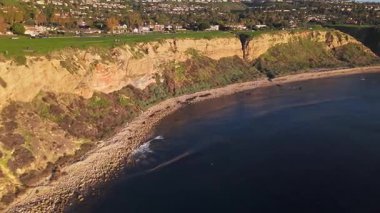 Güneş batarken, okyanusun üzerindeki engebeli kayalıkları ve evleri aydınlatan, nefes kesici Lunada Körfezi 'nin hava yörüngesi çekimi, Palos Verdes Evleri, Kaliforniya