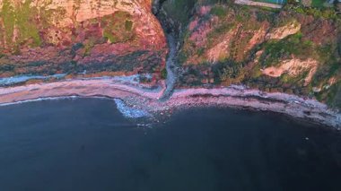 Güneş batarken nefes kesen Lunada Körfezi Kanyonu 'nun hava üssü okyanusun üzerindeki engebeli kayalıkları ve evleri aydınlatıyor, Palos Verdes Evleri, Kaliforniya