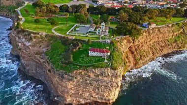 Los Angeles, Kaliforniya 'daki Point Fermin Deniz Feneri' nin hava yörüngesi görüntüsü. Renkli gökyüzü, engebeli uçurumlar ve kıyı boyunca dalgalar çarpıyor.