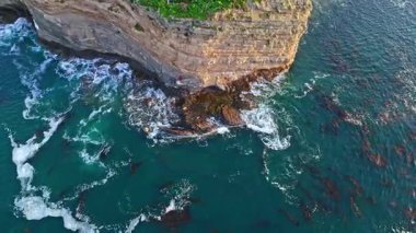 Los Angeles, Kaliforniya 'daki Point Fermin Deniz Feneri' nin sinematik hava yörüngesinde altın saatinde renkli gökyüzü, engebeli uçurumlar ve kıyı boyunca dalgaların çarpıştığı görülüyor.