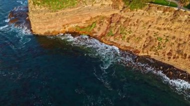 Los Angeles, Kaliforniya 'daki Point Fermin Deniz Feneri' nin sinematik hava yörüngesinde altın saatinde renkli gökyüzü, engebeli uçurumlar ve kıyı boyunca dalgaların çarpıştığı görülüyor.