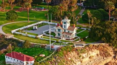 Los Angeles, Kaliforniya 'daki Point Fermin Deniz Feneri' nin telefoto hava yörüngesi. Renkli gökyüzü, engebeli uçurumlar ve kıyı boyunca dalgalar çarpışıyor.