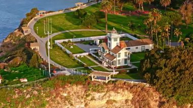 Los Angeles, Kaliforniya 'daki Point Fermin Deniz Feneri' nin telefoto hava yörüngesi. Renkli gökyüzü, engebeli uçurumlar ve kıyı boyunca dalgalar çarpışıyor.