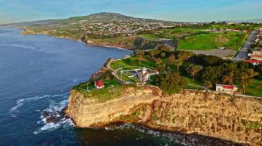 Los Angeles, Kaliforniya 'daki Point Fermin Deniz Feneri' nin, renkli gökyüzü, engebeli uçurumlar ve kıyıya vuran dalgalarla dolu altın saatinde havadan çekilmiş görüntüleri.