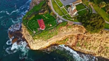 Los Angeles, Kaliforniya 'daki Point Fermin Deniz Feneri' nin sinematik hava gösterimi. Renkli gökyüzü, engebeli uçurumlar ve sahil boyunca dalgalar çarpışıyor.