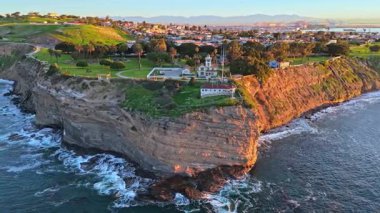 Los Angeles, Kaliforniya 'daki Point Fermin Deniz Feneri' nin renkli gökyüzü, engebeli uçurumlar ve sahil boyunca dalgaların çarptığı hava yörüngesi görüntüsü.
