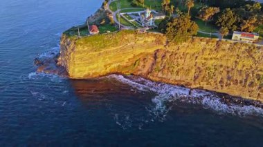 Los Angeles, Kaliforniya 'daki Point Fermin Deniz Feneri' nin renkli gökyüzü, engebeli uçurumlar ve sahil boyunca dalgaların çarptığı sinematik hava gösterimi.