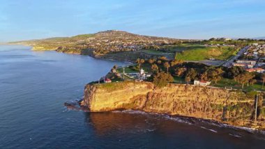 Los Angeles, Kaliforniya 'daki Point Fermin Deniz Feneri' nin renkli gökyüzü, engebeli uçurumlar ve kıyıya vuran dalgalarla gün doğumunda çekilen hava çekimi.