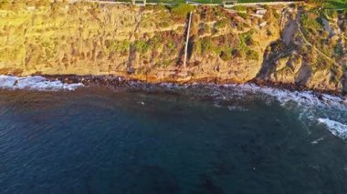 San Pedro, Kaliforniya 'nın engebeli uçurumlarıyla gün doğumunda çekilen hava aracı çekimi ve sahil boyunca dalgalar çarpışıyor.