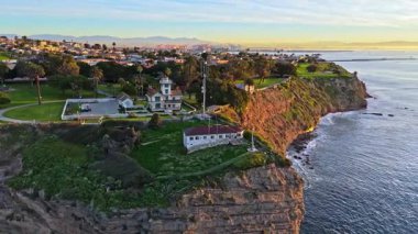 Los Angeles, Kaliforniya 'daki Point Fermin Deniz Feneri' nin alçak hava yörünge görüntüsü. Renkli gökyüzü, engebeli uçurumlar ve kıyıya vuran dalgalar.