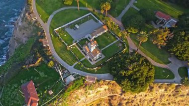 Los Angeles, Kaliforniya 'daki Point Fermin Deniz Feneri' nin renkli gökyüzü, engebeli uçurumlar ve kıyıya vuran dalgalarla çekilen sinematik görüntüsü.