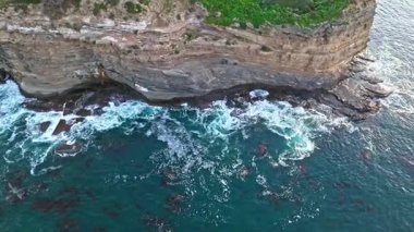 Los Angeles, Kaliforniya 'daki Point Fermin Deniz Feneri' nin sinematik hava yörüngesinde altın saatinde renkli gökyüzü, engebeli uçurumlar ve kıyı boyunca dalgaların çarpıştığı görülüyor.