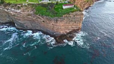 Los Angeles, Kaliforniya 'daki Point Fermin Deniz Feneri' nin sinematik hava yörüngesinde altın saatinde renkli gökyüzü, engebeli uçurumlar ve kıyı boyunca dalgaların çarpıştığı görülüyor.