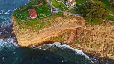 Los Angeles, Kaliforniya 'daki Point Fermin Deniz Feneri' nin sinematik görüntüsü. Renkli gökyüzü, engebeli uçurumlar ve sahil boyunca dalgalar çarpışıyor.