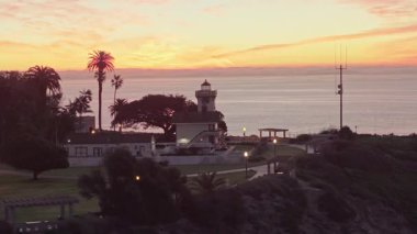 Los Angeles, Kaliforniya 'daki Point Fermin' in mavi saatinde, renkli gökyüzü, engebeli uçurumlar ve sahil boyunca dalgaların çarptığı telefoto hava yörüngesi görüntüsü.