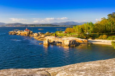 Punta Cabalo 'nun Arousa Adası' ndaki deniz feneri, sahil ve orman manzarası.