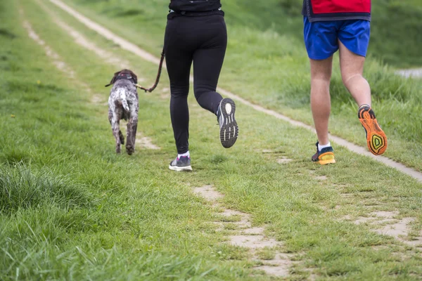 Joven hombre y mujer corriendo con perro — Foto de Stock