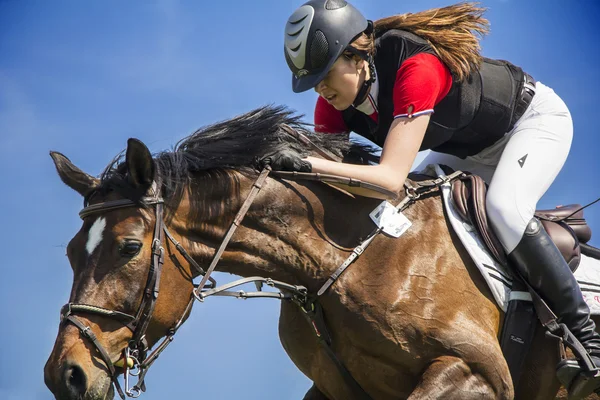 Cavaleira no cavalo marrom no salto sobre um obstáculo — Fotografia de Stock