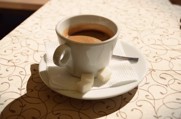 Kop warme koffie op een schoteltje staat op een patroon tafelkleed vintage — Stockfoto