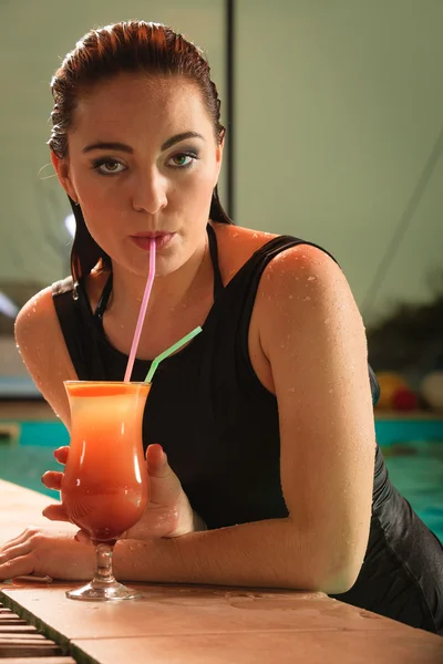 Woman drinking cocktail at swimming pool edge. — Stock fotografie