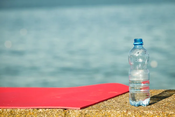 Pink sport mat and water bottle outdoor on sea shore — Stock Photo, Image