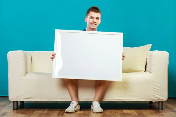 Man on sofa holding blank presentation board — Stock Photo, Image