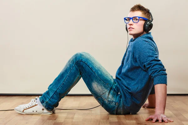 Молодой человек в наушниках сидит на полу — стоковое фото