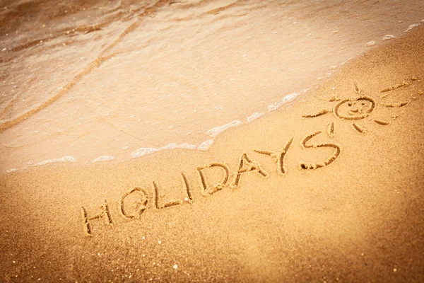 La palabra vacaciones escrita en la arena en una playa —  Fotos de Stock