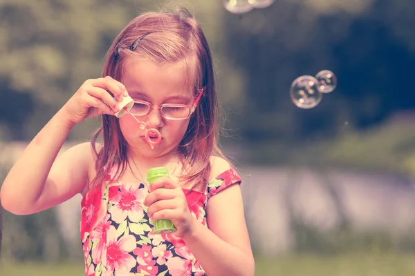 Lilla flickan barnet blåser såpbubblor utomhus. — Stockfoto