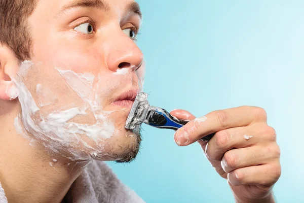 Giovane uomo rasatura utilizzando rasoio con schiuma crema . — Foto Stock