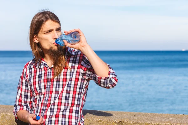 Man long hair relaxing by seaside drinking water — Stock Photo, Image
