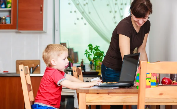 Kleiner Junge mit Laptop und Mutter beim Putzen — Stockfoto