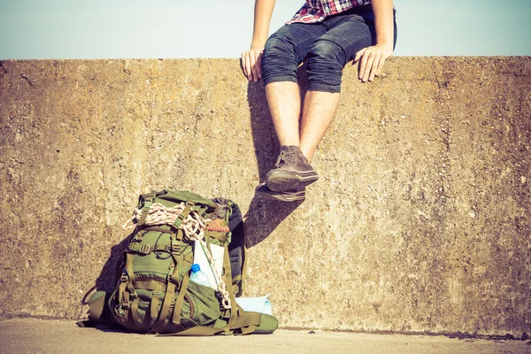 Homem turista mochileiro sentado na parede grunge ao ar livre — Fotografia de Stock