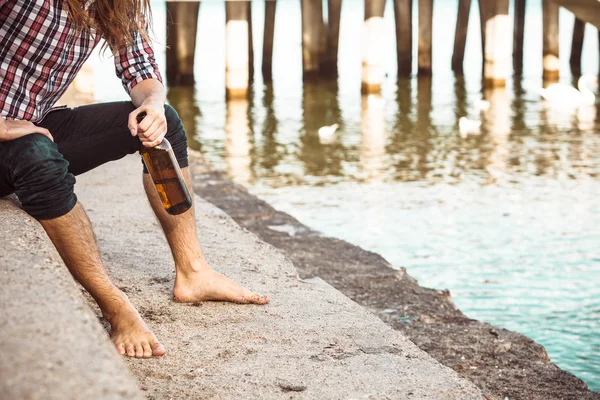 Hombre deprimido con botella de vino sentado en la playa al aire libre — Foto de Stock