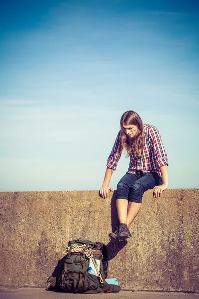 Man tourist backpacker sitting on grunge wall outdoor — Stock Photo, Image