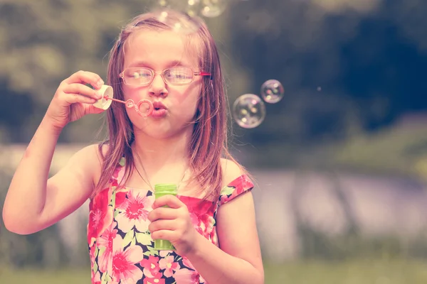 Lilla flickan barnet blåser såpbubblor utomhus. — Stockfoto