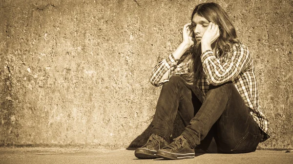 Mann mit langen Haaren sitzt traurig allein auf Grunge-Wand — Stockfoto